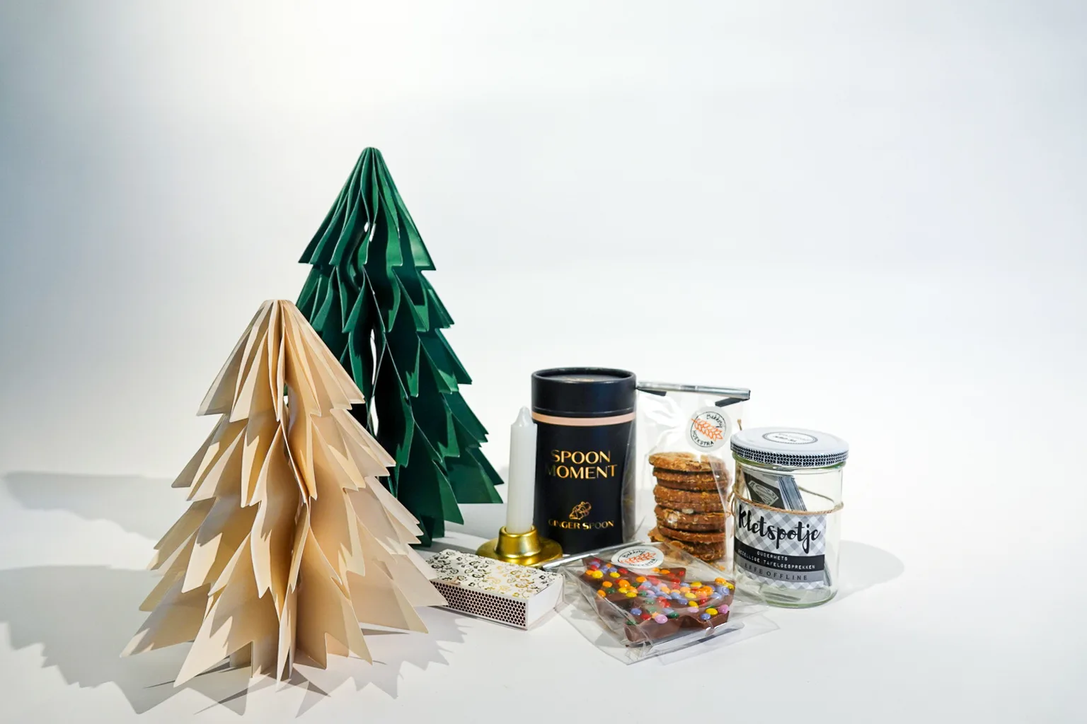 Compact kerstpakket met thee, koekjes en snoep bij een papieren kerstboom