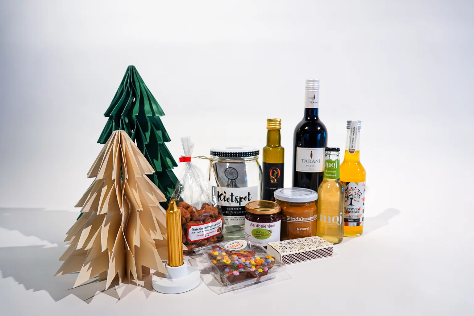 Kerstpakket met een pot met gespreksvragen, een gouden kaars, wijn, limonade, jam en chocolade